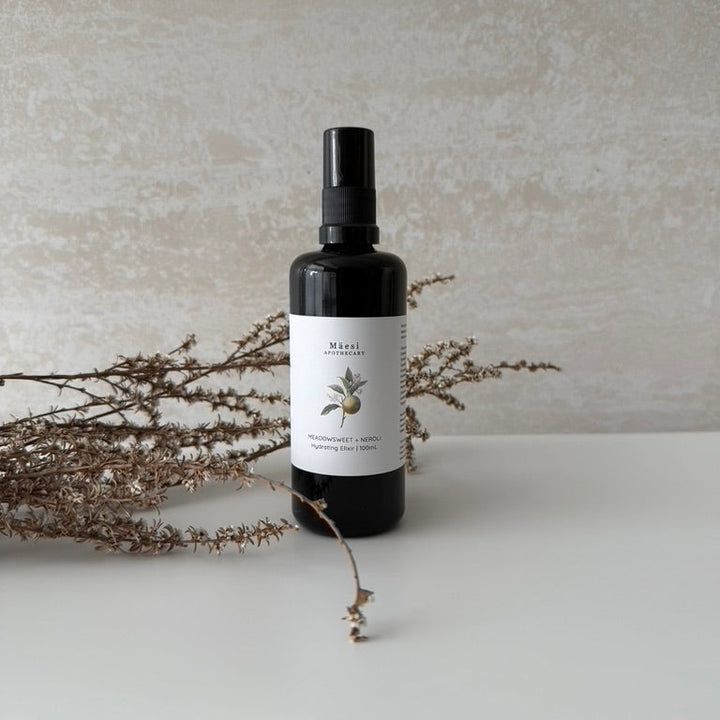 Black spray bottle with a label on a light surface with dried plants.